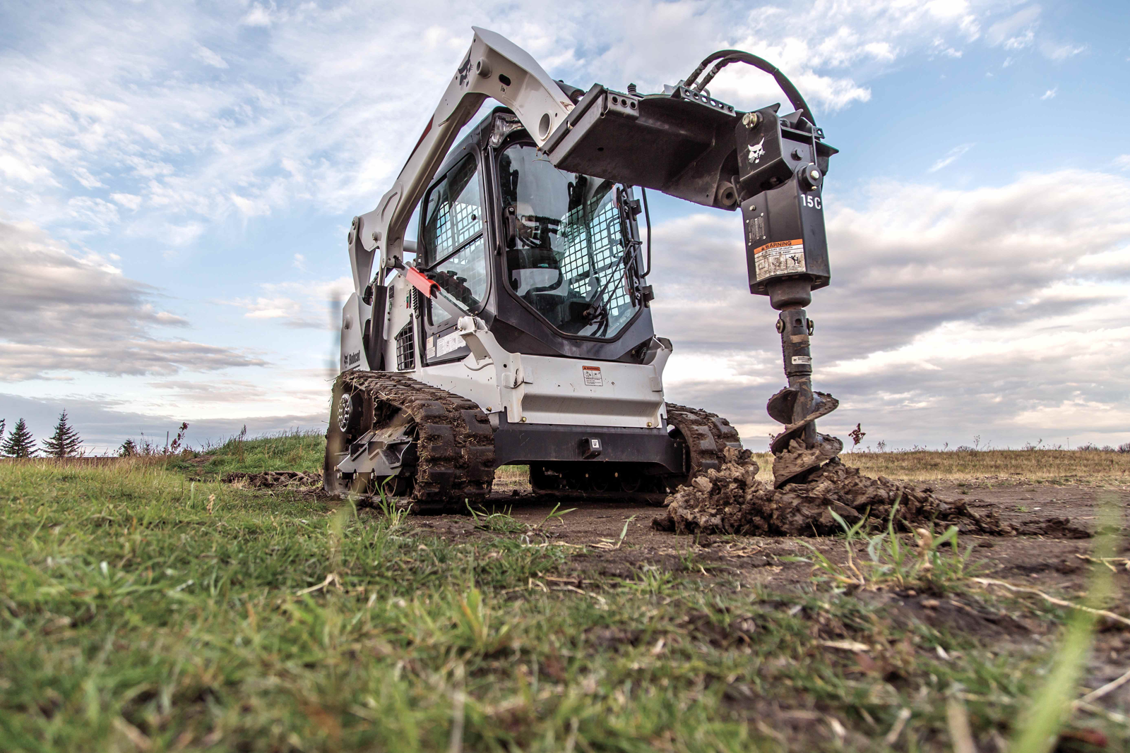 Bobcat with auger drilling foundation boreholes for a greenhouse